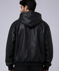 A man viewed from the back wearing a black leather hooded jacket against a plain light gray studio background.